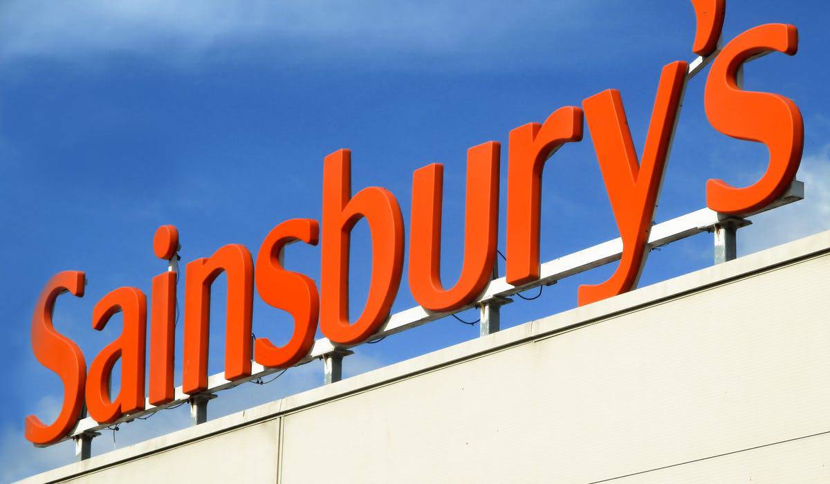 Bright orange "Sainsbury's" sign against a blue sky, mounted on a white building