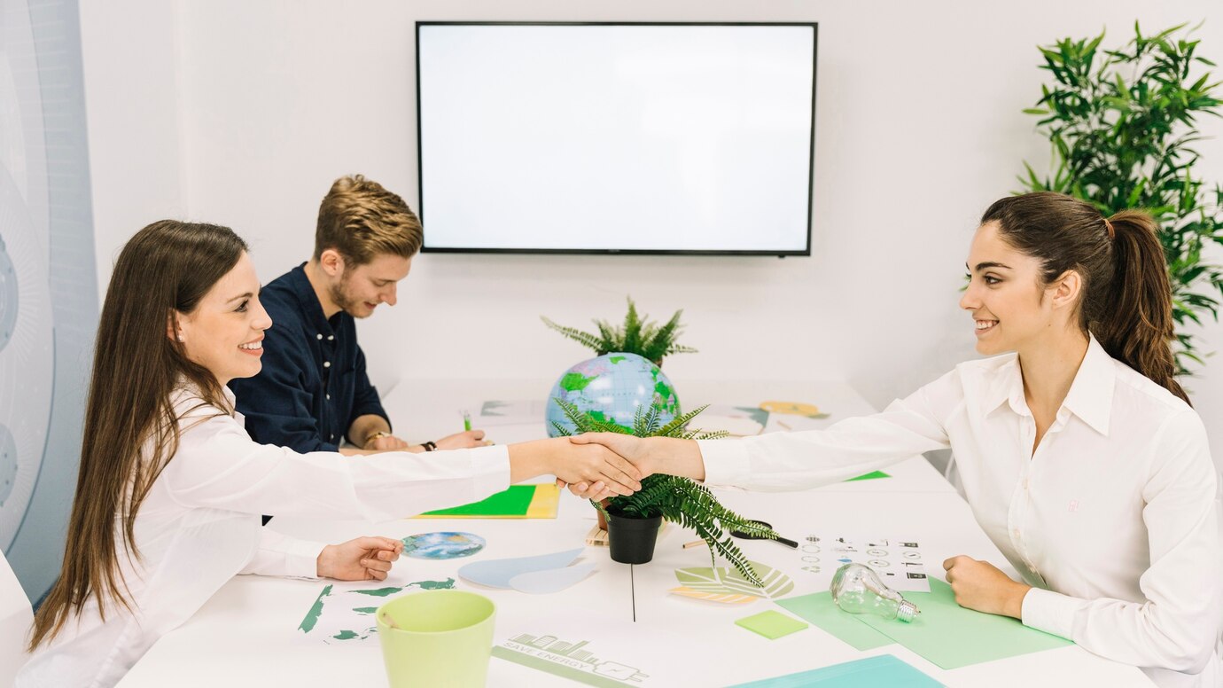  individuals shake hands across a table decorated with eco-themed
