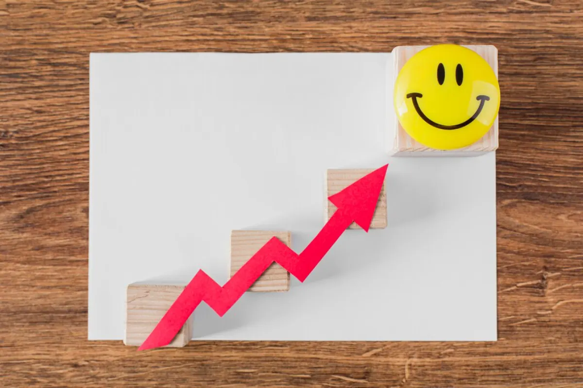 A red arrow graphically ascends wooden blocks toward a yellow smiley face on top, symbolizing growth and positivity on a white sheet.