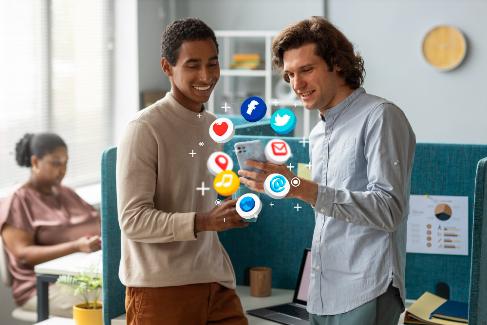 Two individuals in an office setting engage with a smartphone, surrounded by various social media icons and a laptop in the background.