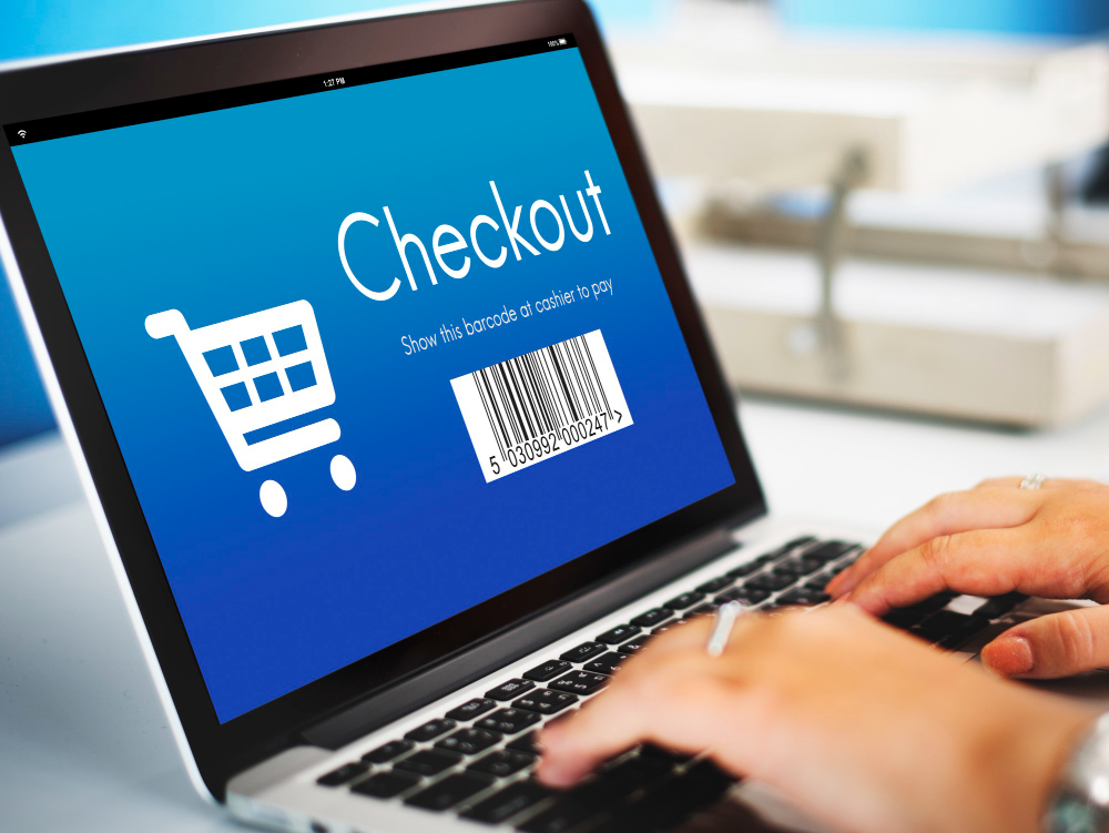 Person typing on a laptop displaying a checkout screen with a shopping cart icon and a barcode for payment.