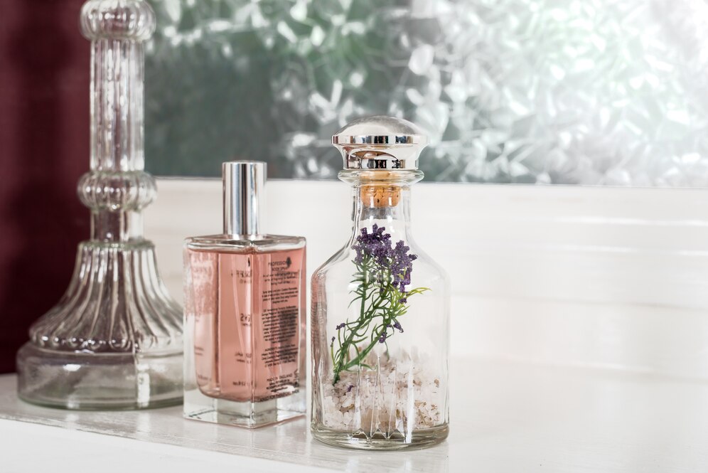 A decorative glass bottle filled with salt and lavender, beside a clear perfume