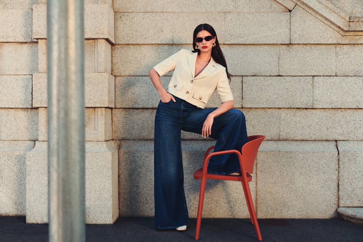 A person poses confidently on a red chair against a textured stone wall